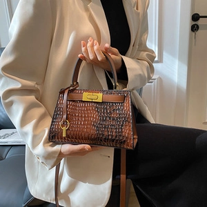 Detail of brown crocodile pattern handbag with gold clasp on white blazer outfit