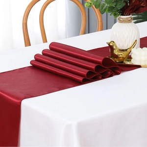 Luxurious wine red satin table runner draped over a white cloth for wedding decor