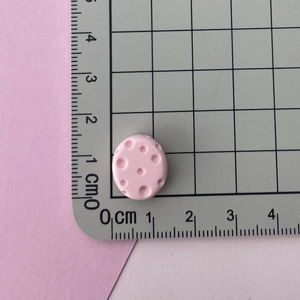 Close-up of a pink resin mini oval button showing dimensions of 1.2cm x 1.5cm on a grid