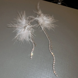 Detail of long tassel earrings with white feathers and shimmering rhinestone accents