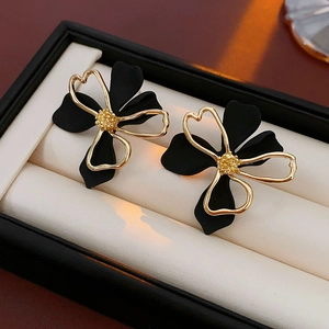Detailed macro of gold-rimmed matte black flower earrings in a premium black gift box