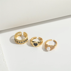Detailed shot of three gold open rings set with blue gemstone, black heart, and pearl
