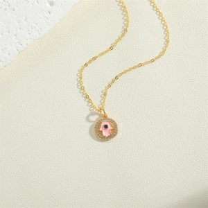 Gold Hamsa necklace with pink enamel pendant and blue gemstone center on white textured wall