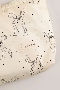 Detailed view of cream canvas makeup bag with black polka dots and bow pattern