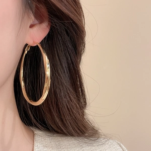 Detail view of large gold hoop earrings with twisted metallic texture on a female model
