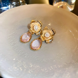 Detailed close-up of gold floral earrings with cat-eye opal stones on ceramic background