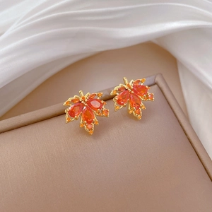 Macro shot of maple leaf stud earrings with orange faceted gemstones in gold setting