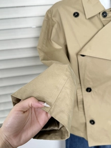 Close-up of khaki short trench coat featuring double-breasted black buttons and cotton twill fabric