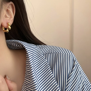 Close-up of golden twisted rope metal hoop earrings worn on a model with a casual outfit