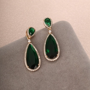 Macro shot of emerald green pear-shaped earrings with white zircon accents in gold