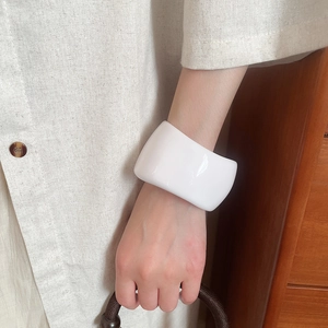 Detailed shot of a wide glossy white resin bangle worn on wrist against a linen outfit