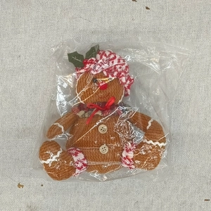 Detail of gingerbread man plush ornament with red plaid hat and bow tie in packaging