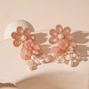 Close-up of elegant pink flower tassel earrings with pearls on a textured stone surface