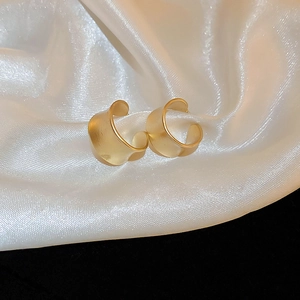 Detailed macro view of matte gold C-shaped earrings on elegant white silk fabric