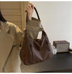 Detail view of brown textured leather hobo bag with vertical zipper pockets and metal hardware