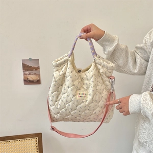 Detail of floral quilted handbag featuring woven handles and adjustable pink shoulder strap