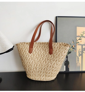 Detail of woven straw tote bag with brown PU leather handles on a minimalist table