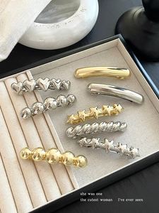 Macro shot of assorted gold and silver spring hair clips in a beige velvet jewelry box