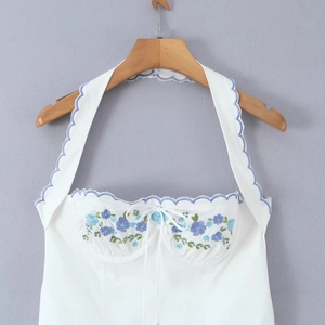White halter top with blue floral embroidery and scalloped edges on wooden hanger