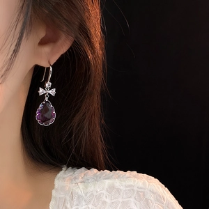 Vue rapprochée de boucles d'oreilles nœud en argent avec une gemme goutte violette