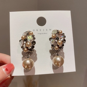 Macro detail of champagne gold floral earrings with pearls and rhinestones held by hand
