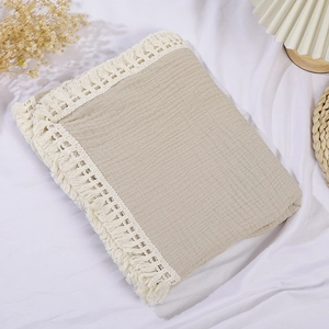 Detailed view of beige muslin baby blanket featuring white lace trim and fringe edges