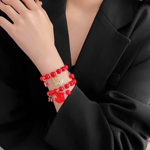 Détail d'un bracelet en perles rouges avec breloques dragon porté sur une veste noire