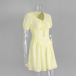 Detail of yellow cotton dress featuring intricate hollow embroidery and V-neck tie closure
