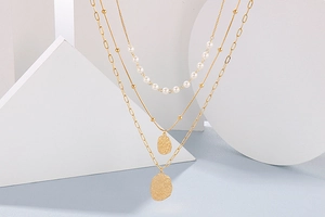 Detail of layered gold necklace featuring pearls and textured hammered coin pendants