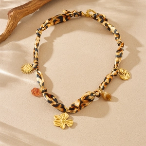 Chic leopard print silk scarf necklace with golden sun and floral charms on sand surface