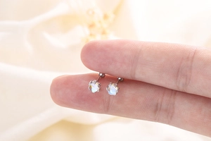 Close-up of S925 sterling silver moonstone stud earrings held between fingertips