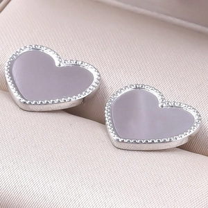 Macro shot of silver heart stud earrings with milgrain edge on beige velvet