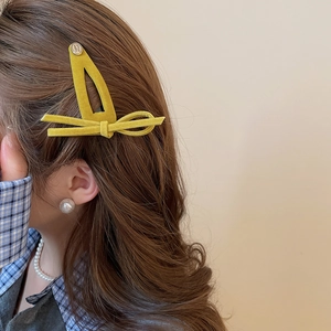Detail of yellow flocked bow hair clip with engraved smile metal button on hair
