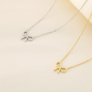 Close-up of minimalist bow necklaces in gold and silver finishes on a soft fabric background