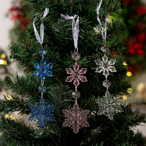 Three colorful acrylic snowflake ornaments in blue, pink, and clear hanging on a Christmas tree