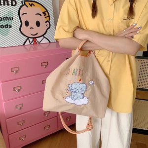 Close-up of beige tote bag featuring blue elephant embroidery and orange rope handles
