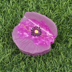 Poppy flower hair claw clip in purple and pink acetate, top view on green grass