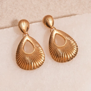 Detailed view of golden teardrop earrings with radial texture on white marble stone