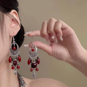 Detail of bohemian tassel earrings with hollow silver rings and red beads on ear hook
