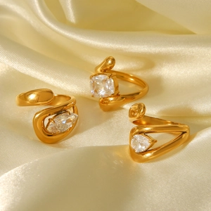 Three gold rings with teardrop and square crystals on a cream silk background