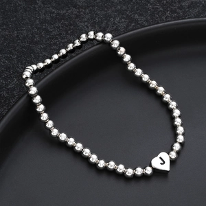 Close-up of beaded silver heart bracelet with engraved letter J on dark background