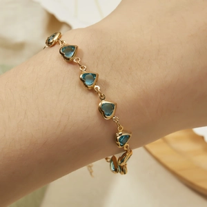 Detail of a golden chain bracelet featuring elegant transparent blue heart-shaped gems