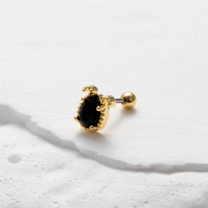 Dettaglio macro di orecchino a goccia dorato con zircone nero su sfondo strutturato