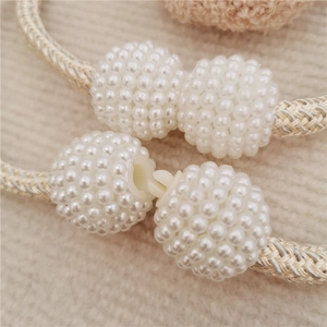 Detail of beige woven ropes with faux pearl beads and plastic buckles for curtains