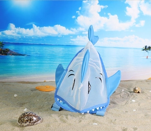 Blue shark-shaped mesh beach bag for kids on a sunny seaside beach background