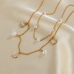 Detailed close-up of double-layered gold necklace with white pearl and shell flower pendant