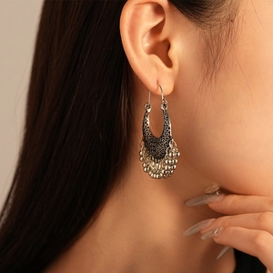 Détail de boucles d'oreilles ethniques argentées avec motif ajouré et pampilles en perles