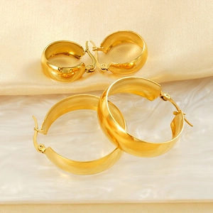 Détail de boucles d'oreilles créoles dorées sur fond de soie beige et texture