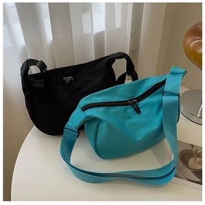Minimalist nylon crescent crossbody bags in black and lake blue on a clean white desk