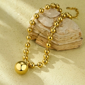Minimalist gold ball pendant necklace with beaded chain on natural sandstone background